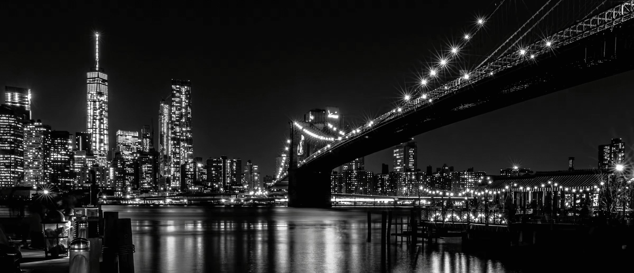 Monochrome cityscape featuring the Brooklyn Bridge's Gothic Revival architecture illuminated against the Manhattan skyline.