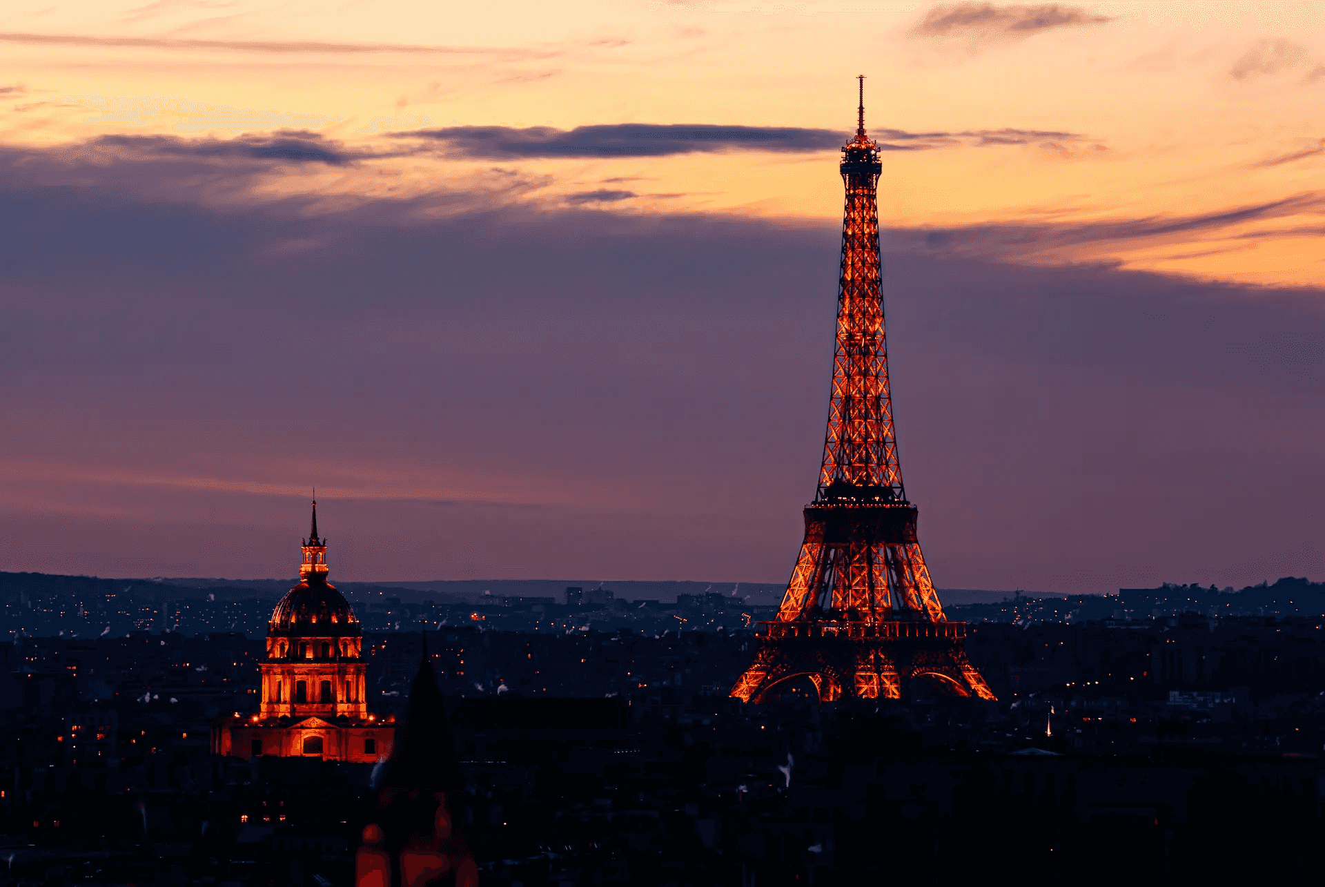 A stunning photograph of the Eiffel Tower and the dome of Les Invalides in Paris, illuminated against a vibrant twilight sky.