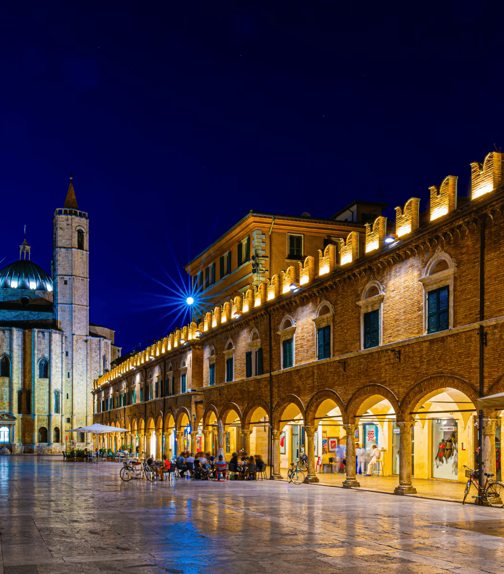 Piazza del Popolo at dusk in Ascoli Piceno, Italy, with illuminated colonnades.