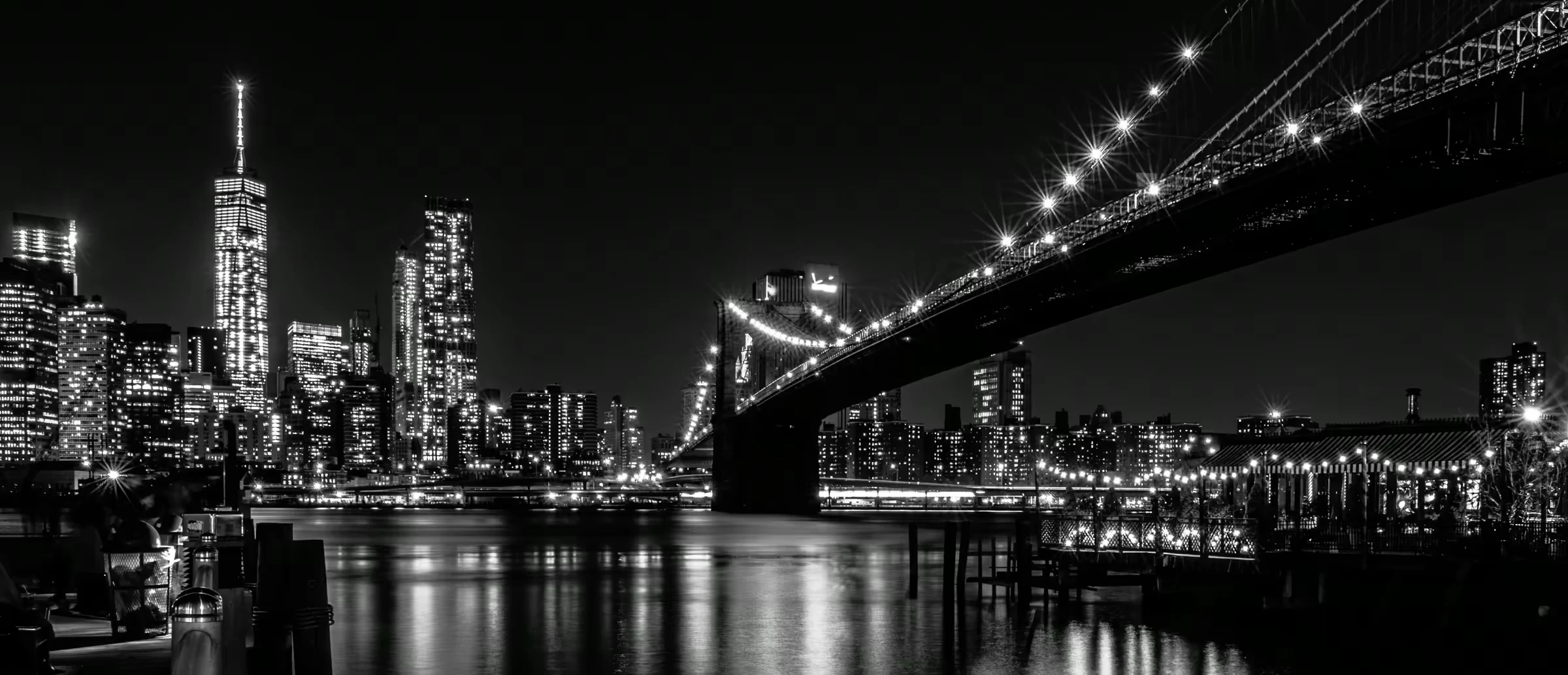Monochrome cityscape featuring the Brooklyn Bridge's Gothic Revival architecture illuminated against the Manhattan skyline.