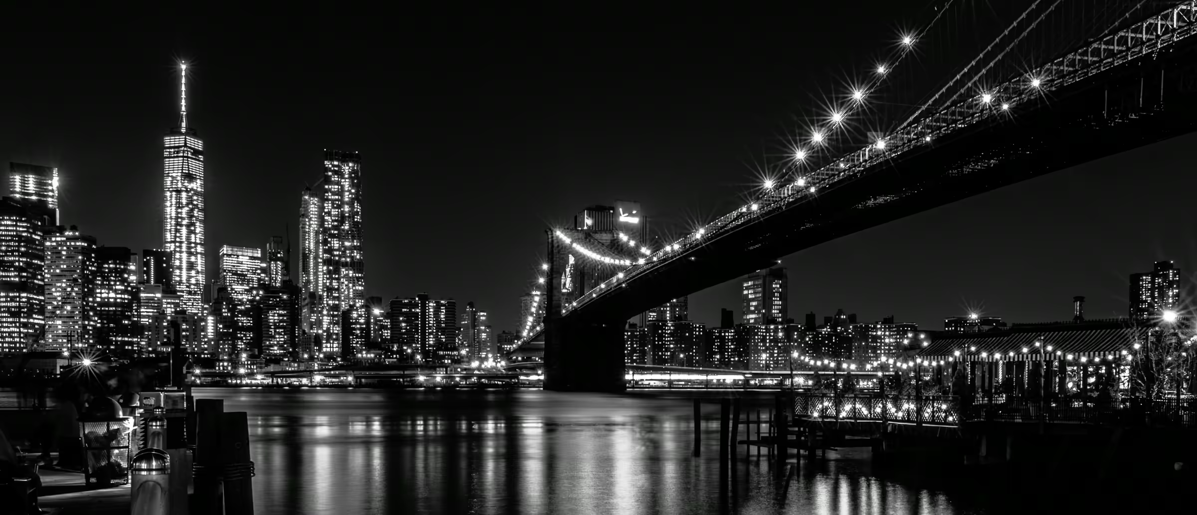 Monochrome cityscape featuring the Brooklyn Bridge's Gothic Revival architecture illuminated against the Manhattan skyline.