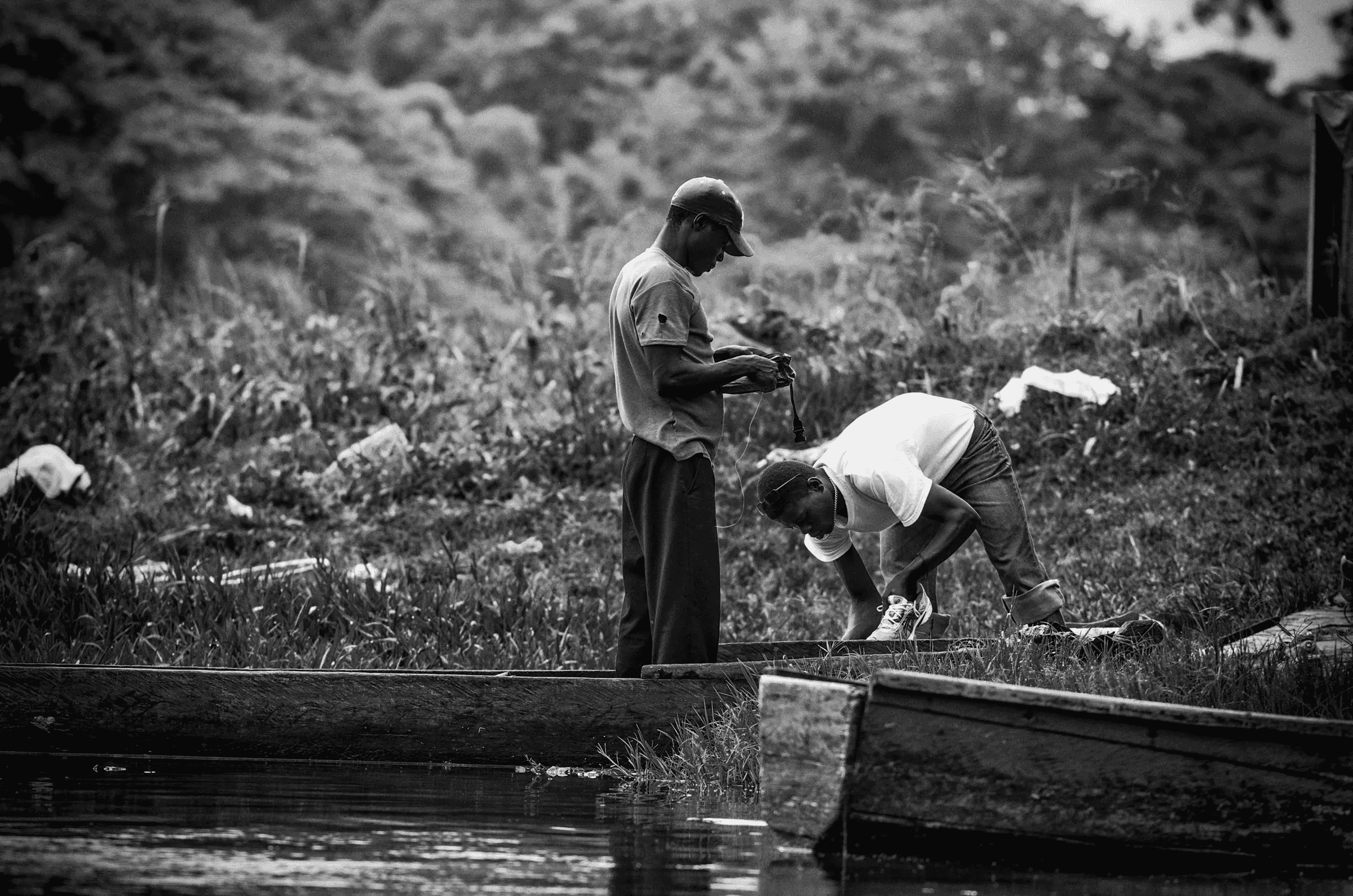 Fishermen's Preparations Two men working on or near simple boats/canoes on a riverbank, possibly preparing fishing gear.