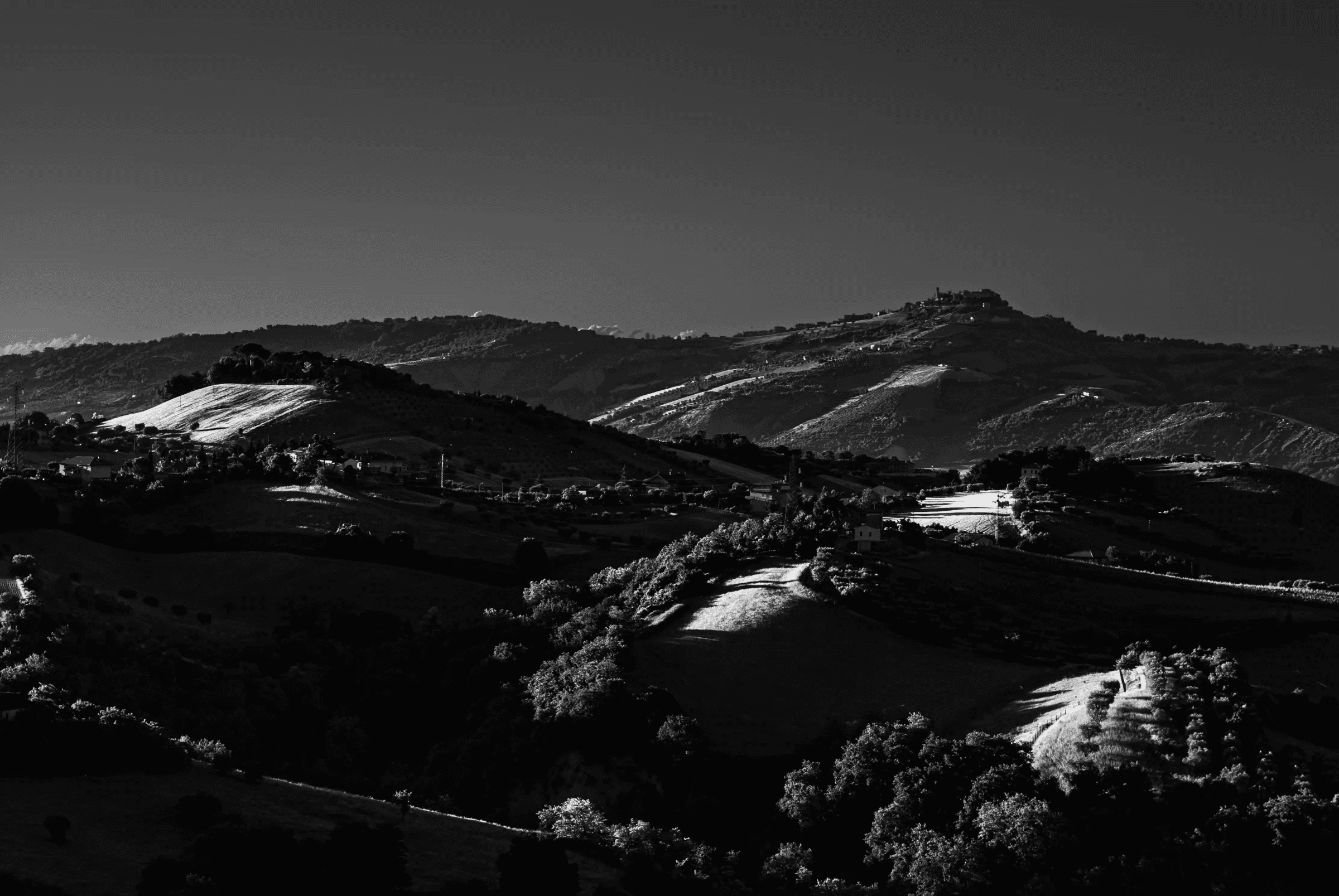 Black and white landscape photograph of rolling hills in central Italy, view towards Colonnella from the Marche/Abruzzo region, showing strong contrast between light and shadow.