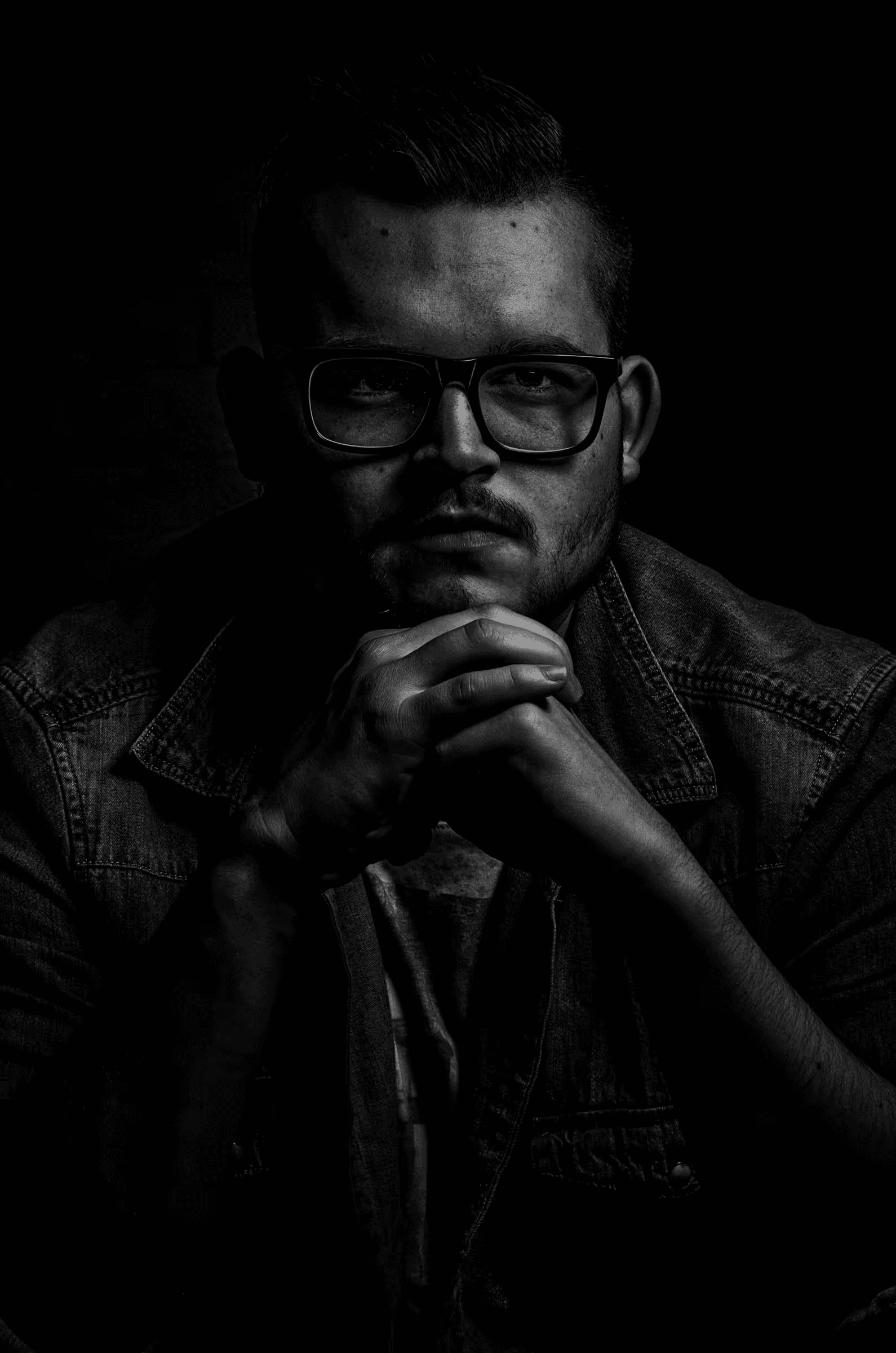Low-key black and white portrait photograph of a man wearing glasses.