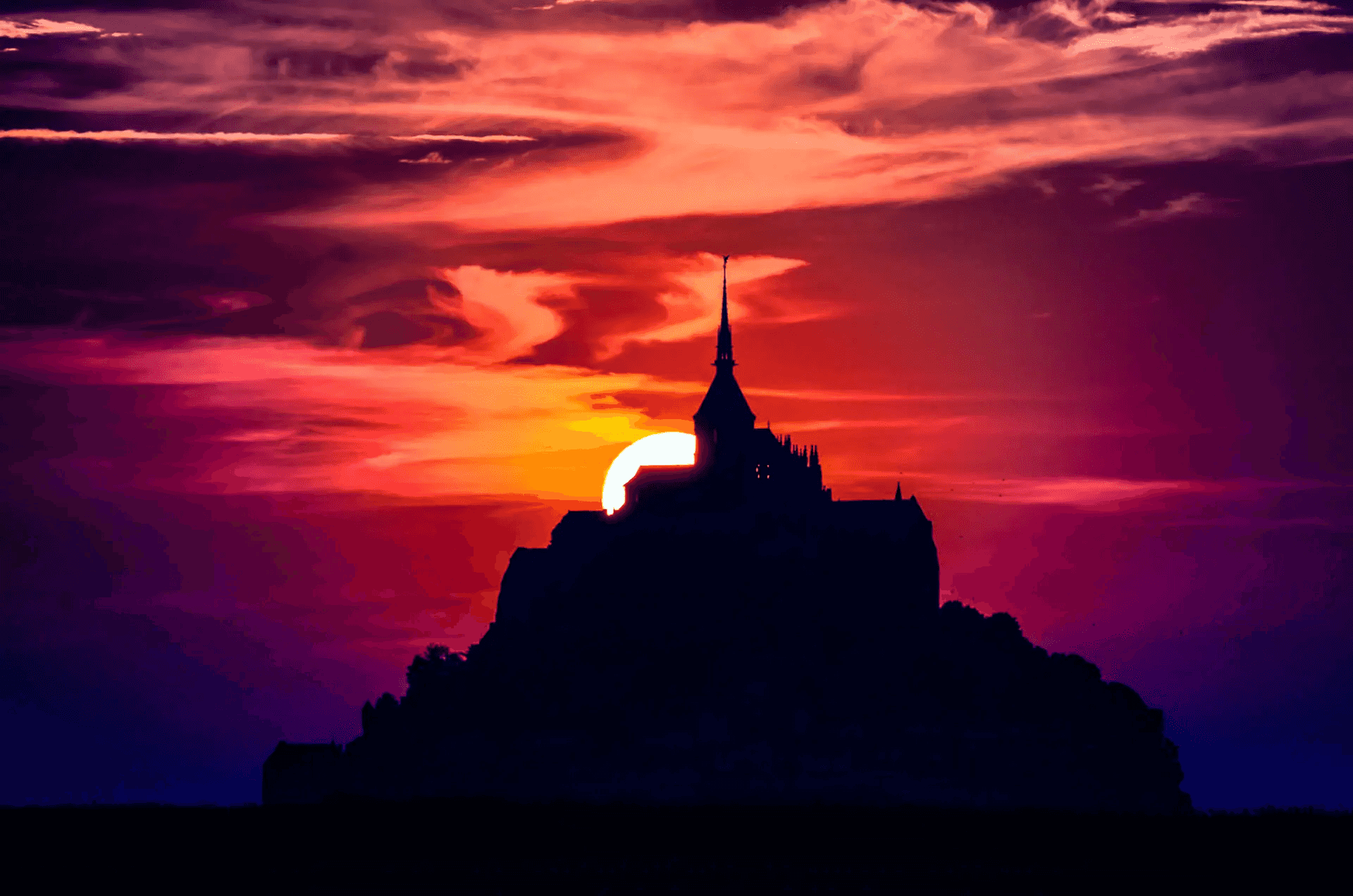 Silhouette of Mont Saint-Michel, France, at sunset. The dark shape of the island abbey is sharply contrasted against a vibrant, fiery sky with hues of red, orange, and purple.