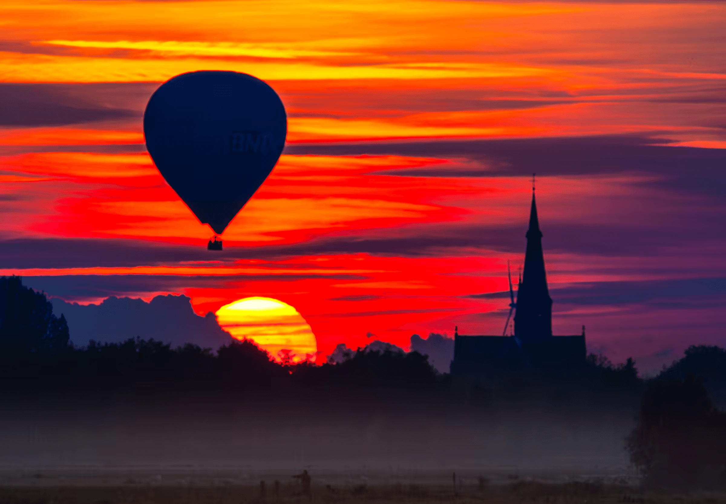 Click to view in fullscreen A hot air balloon silhouetted against a vibrant sunset in North Brabant, Netherlands.
