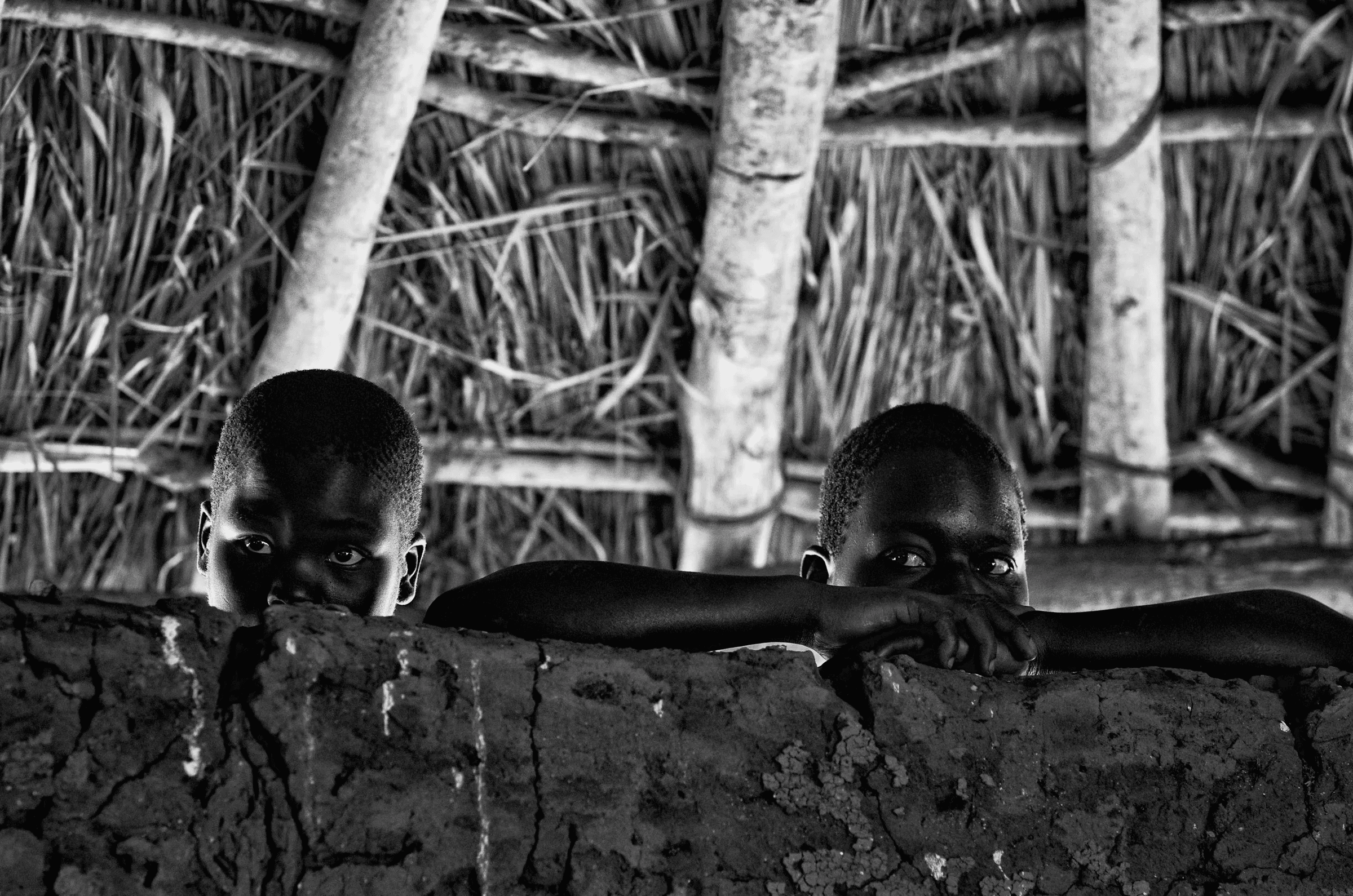 Click to view in fullscreen Peeking Over the Wall in a quiet portrait in North Uganda in monochrome.