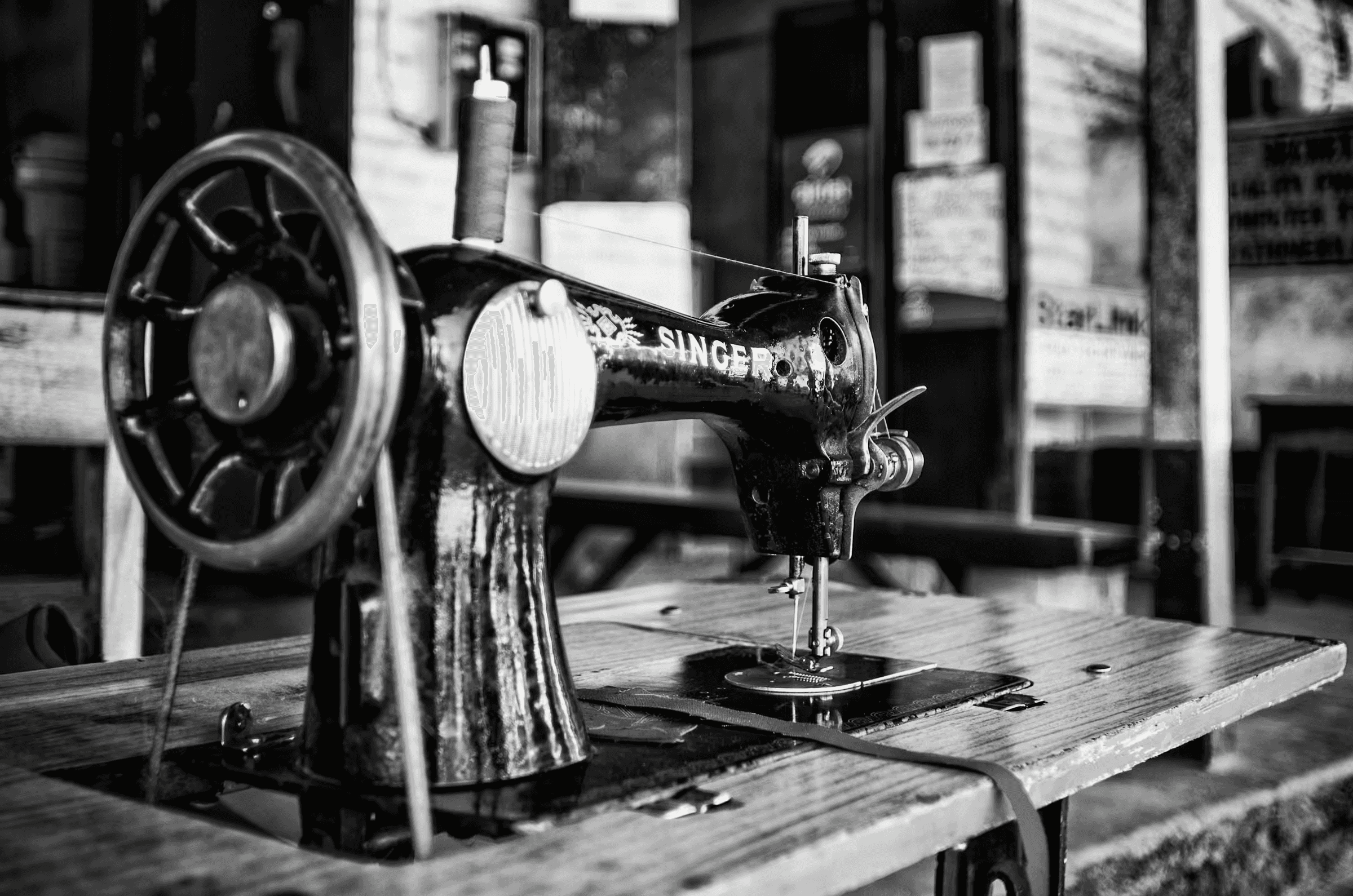 Black and white photograph of a vintage Singer sewing machine in Botswana. The machine, prominently displaying the 'SINGER' logo, sits on a wooden table.