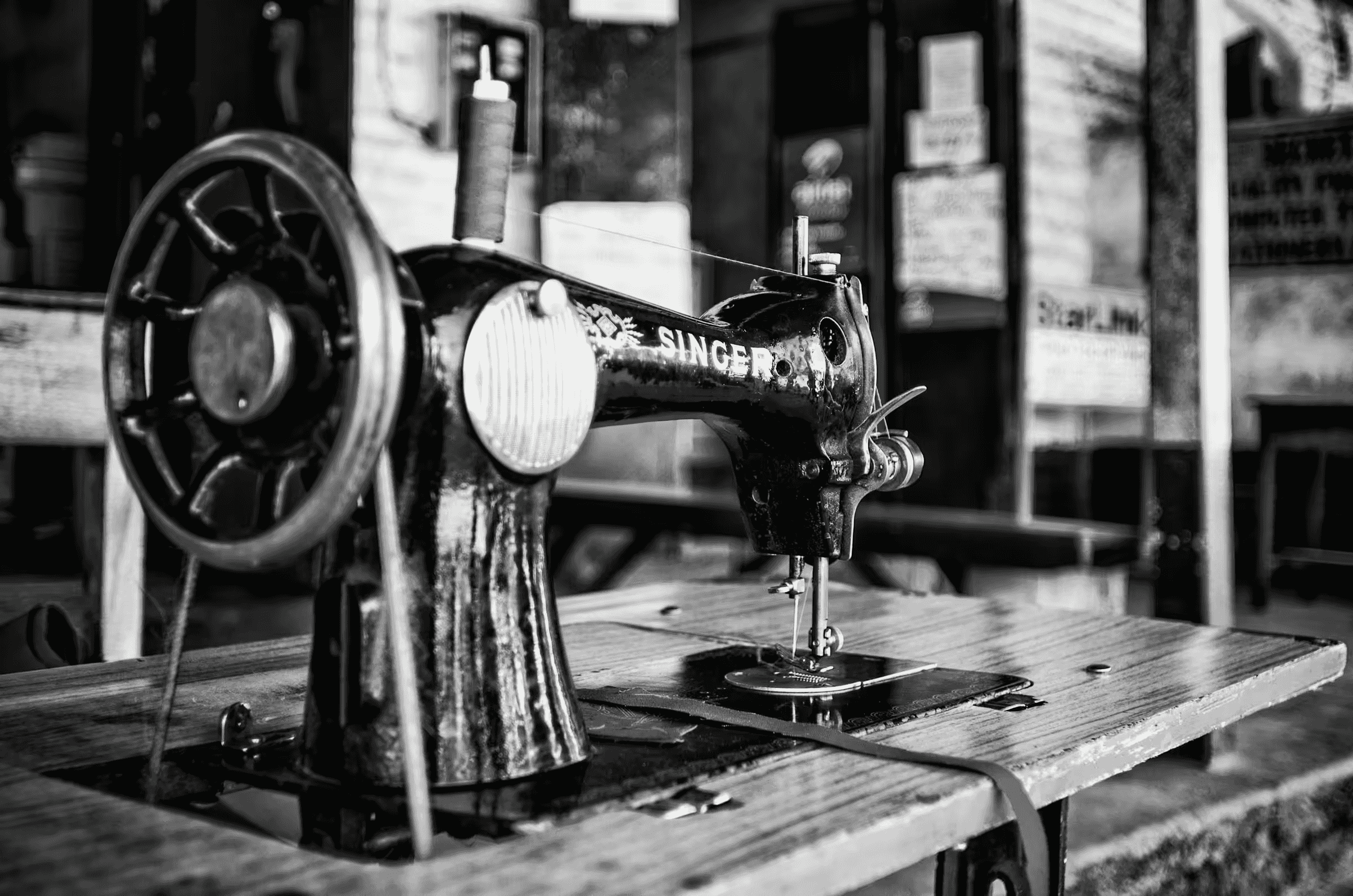 Black and white photograph of a vintage Singer sewing machine in Botswana. The machine, prominently displaying the 'SINGER' logo, sits on a wooden table.