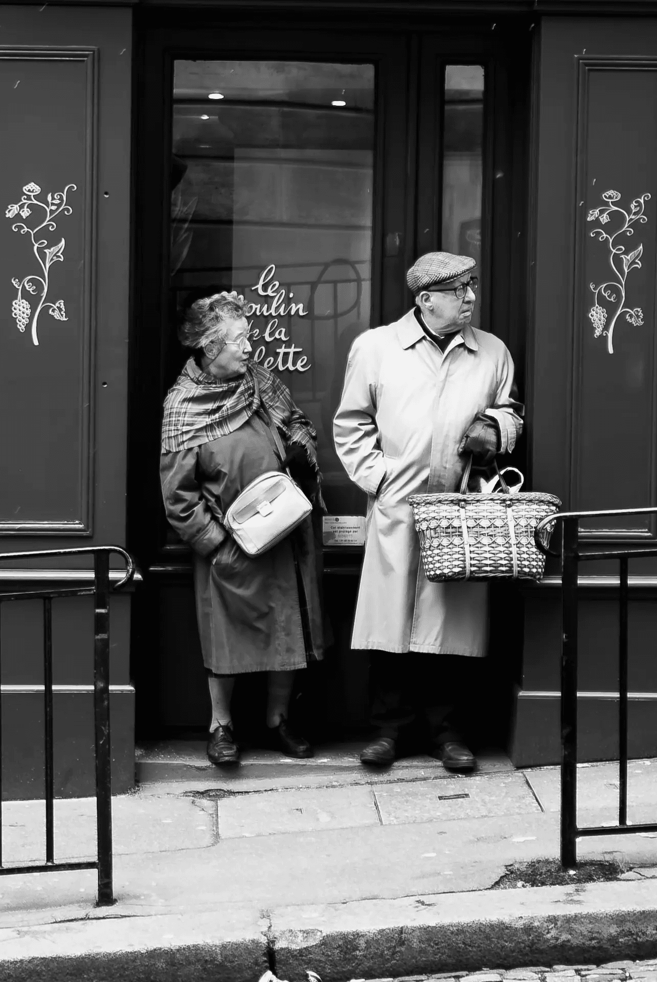 An elderly couple standing in the doorway of a Parisian shop.