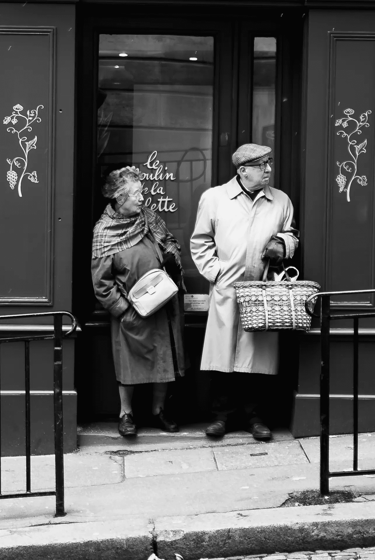 An elderly couple standing in the doorway of a Parisian shop.