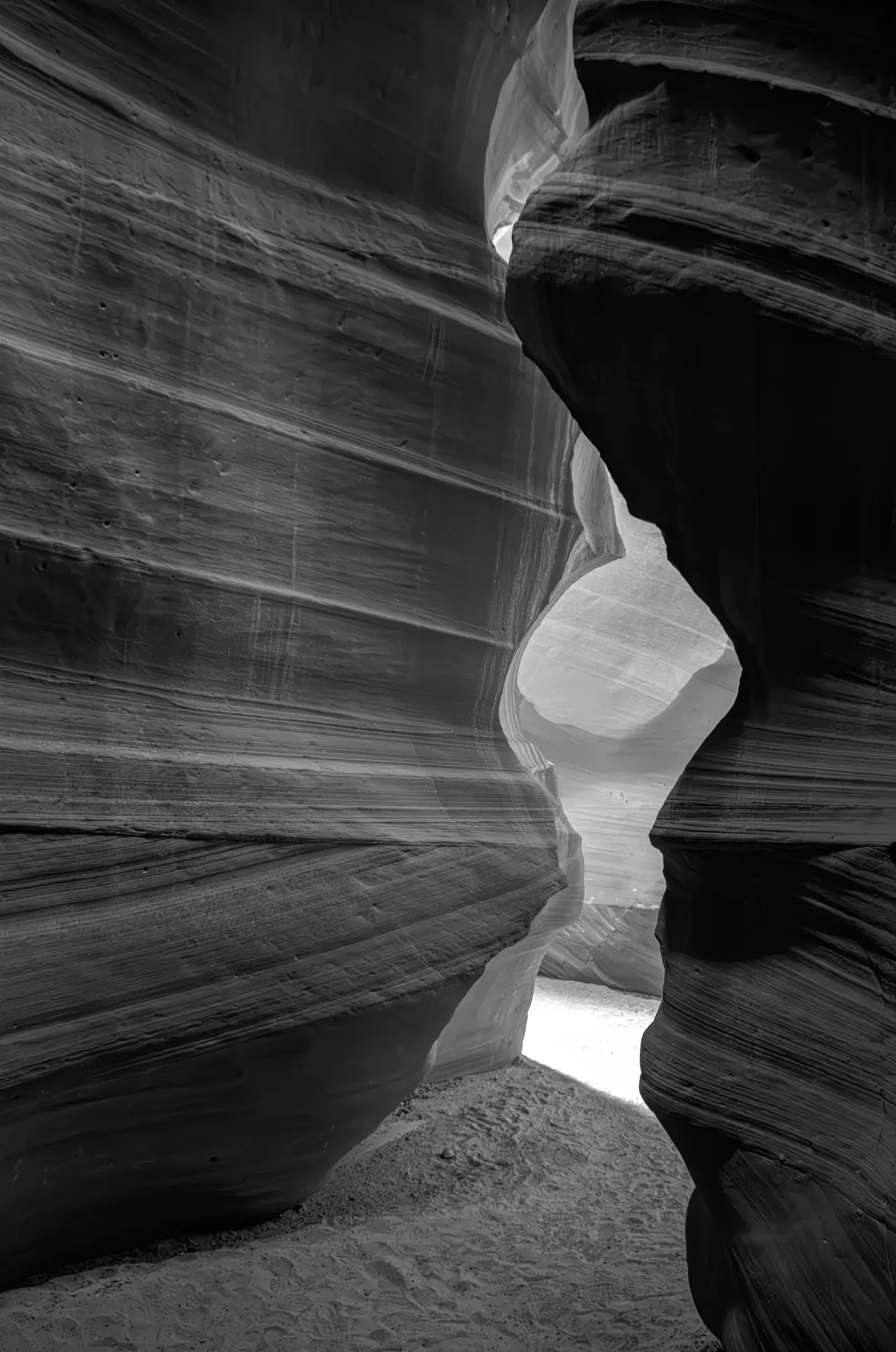Black-and-white view through the curved, layered sandstone walls of Antelope Canyon in Arizona, with daylight entering through a narrow opening.