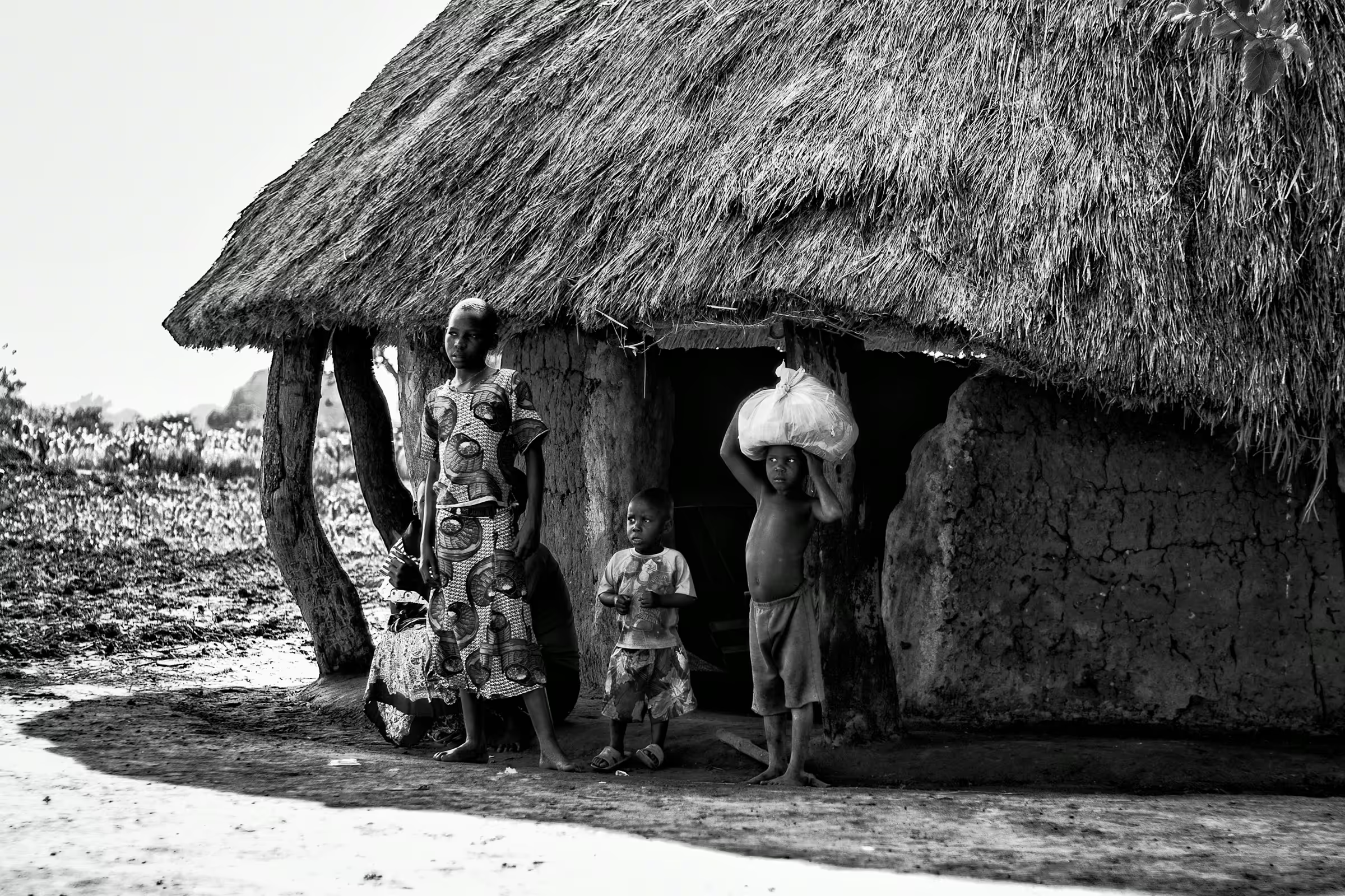 A Ugandan family standing outside their traditional mud hut with a thatched roof.