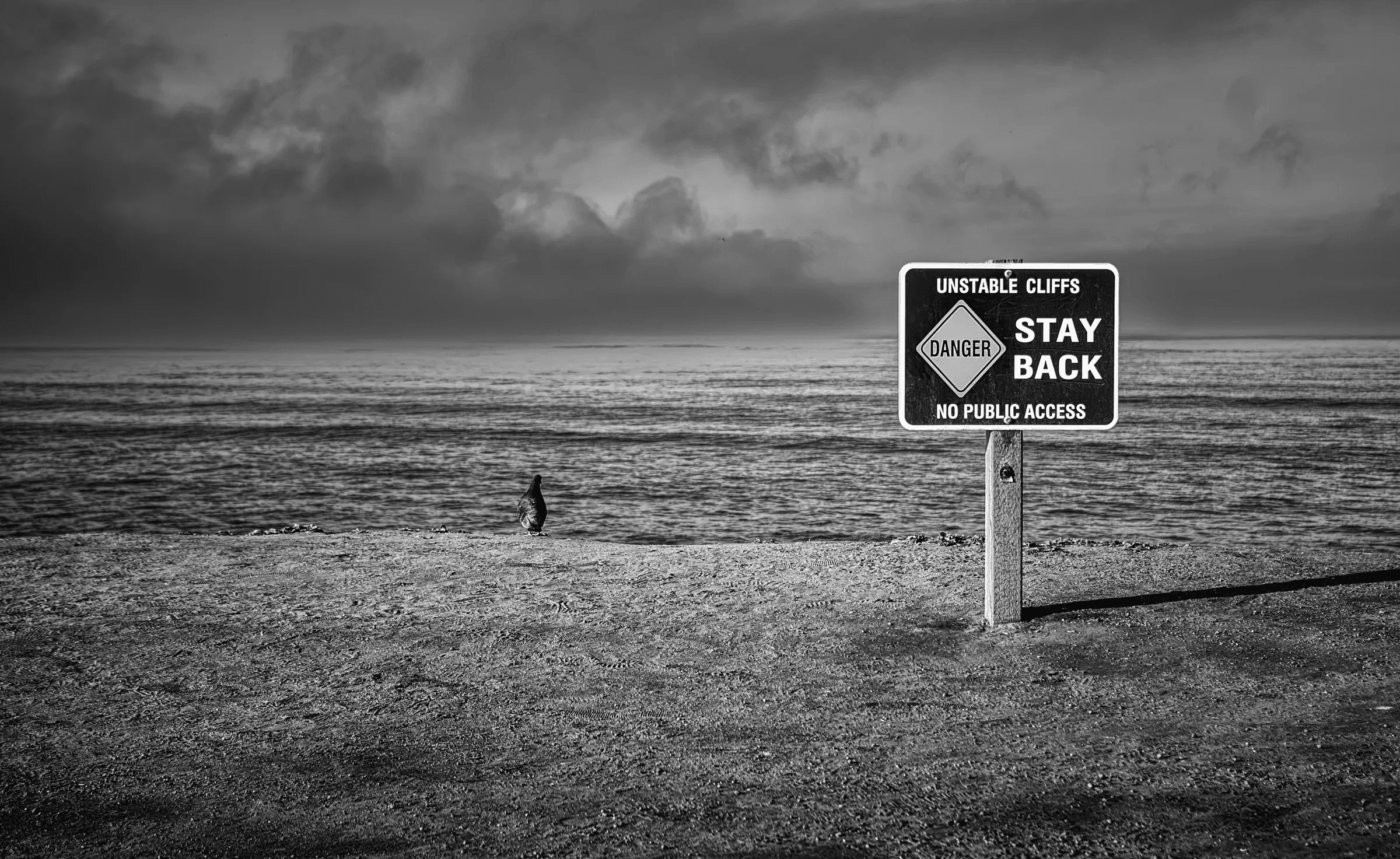 Unstable Cliffs Warning Landscape view of unstable cliffs warning sign coast in monochrome.