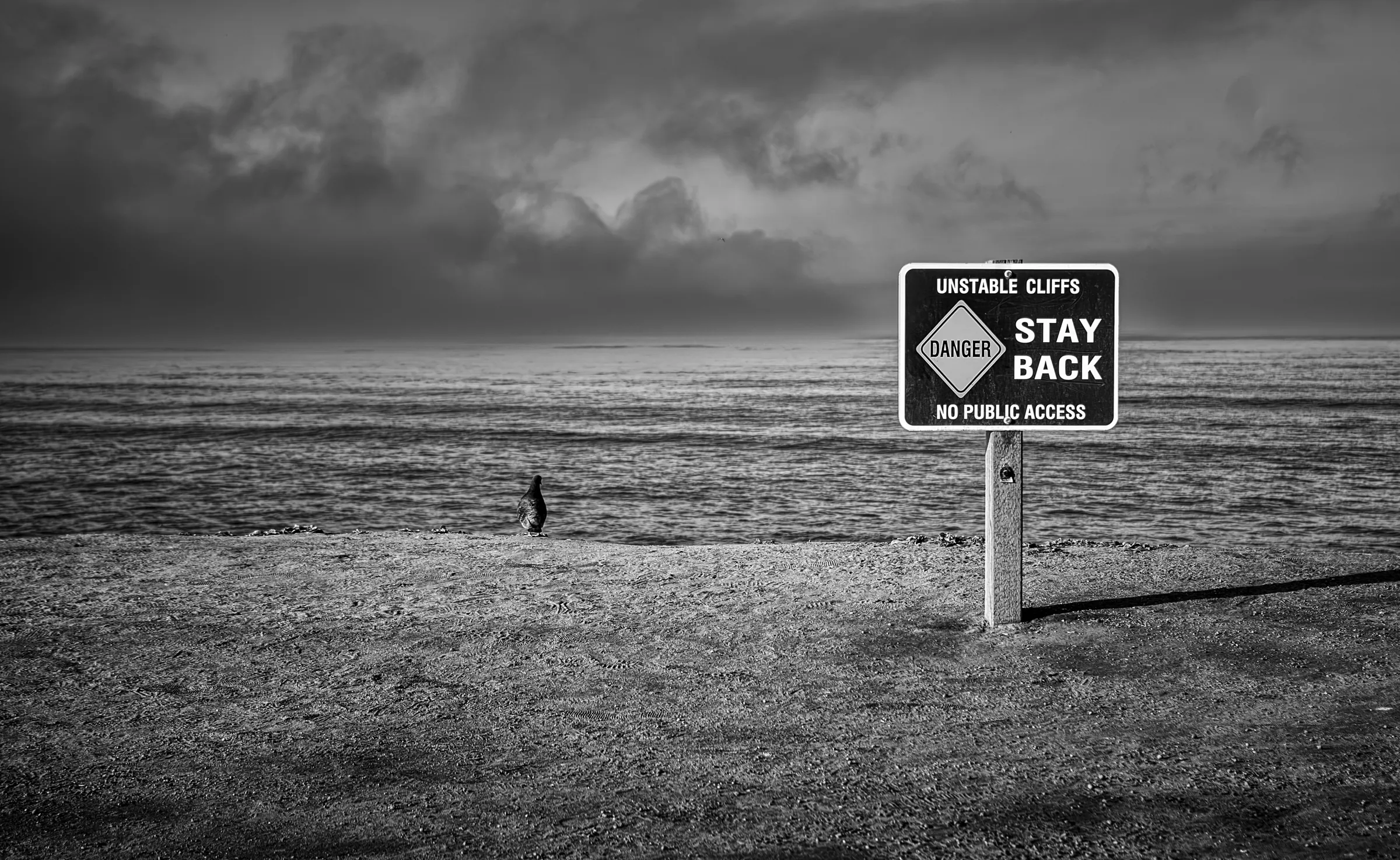 Landscape view of unstable cliffs warning sign coast in monochrome.
