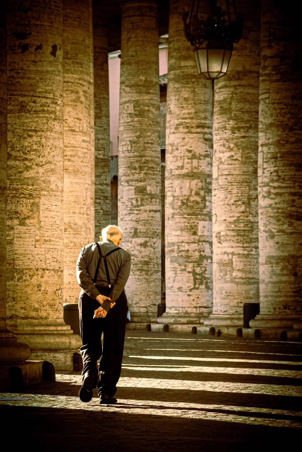 Priest walking beneath the colonnade of St. Peter's in Vatican City.