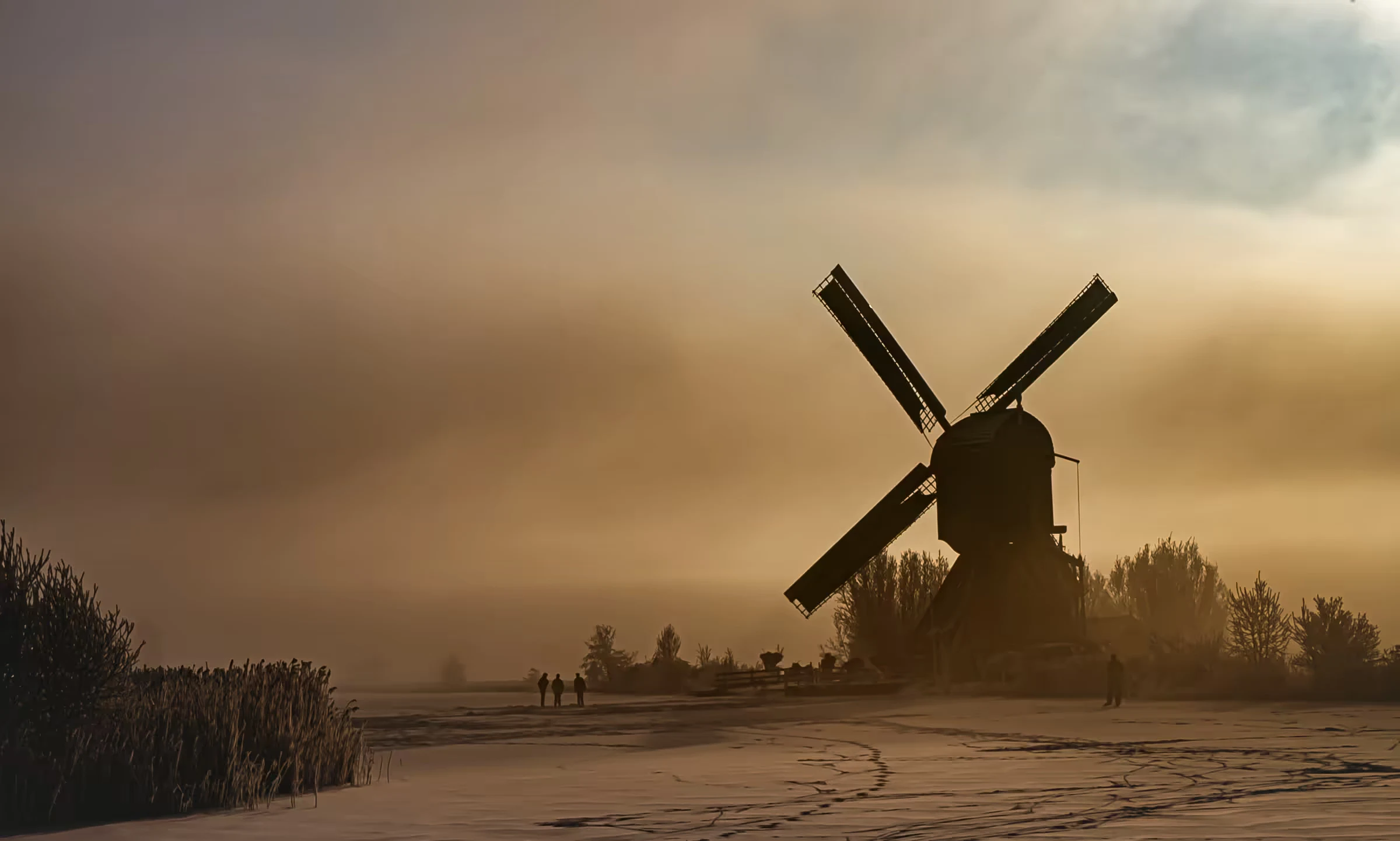 Dutch windmill in golden winter mist at Kinderdijk, silhouetted above a frosted field.